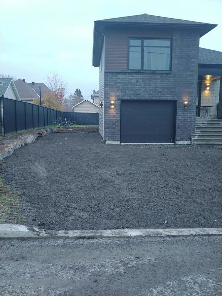 Maison à deux étages avec une porte de garage noire et une allée de gravier vide.