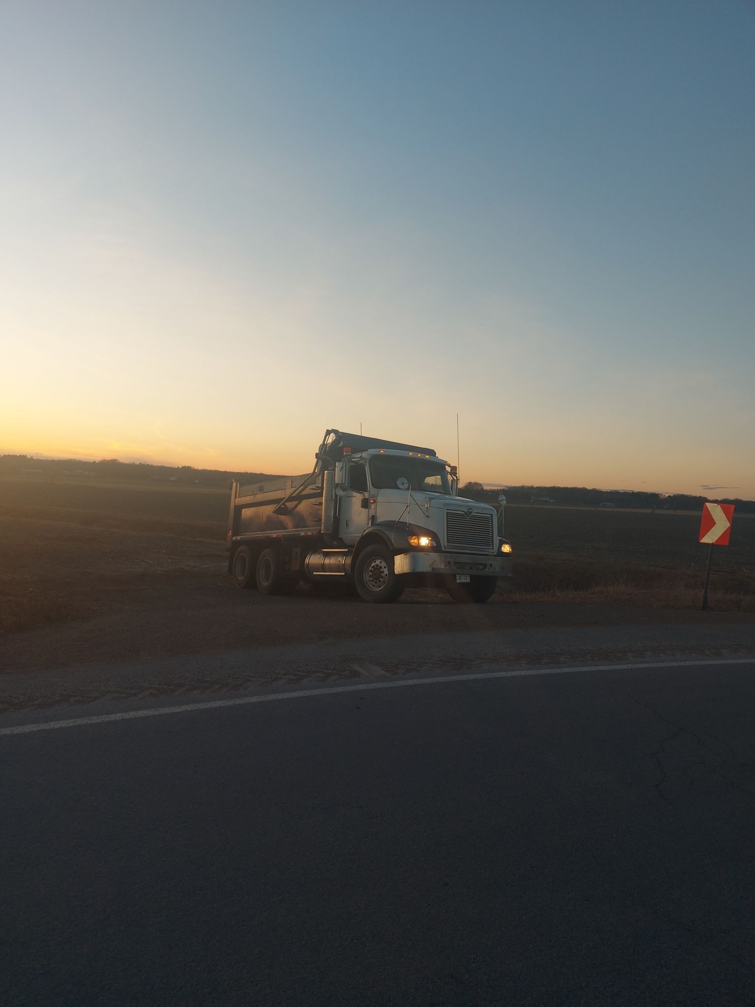 Dépanneuse blanche sur une route de campagne au coucher du soleil ; champs en arrière-plan.