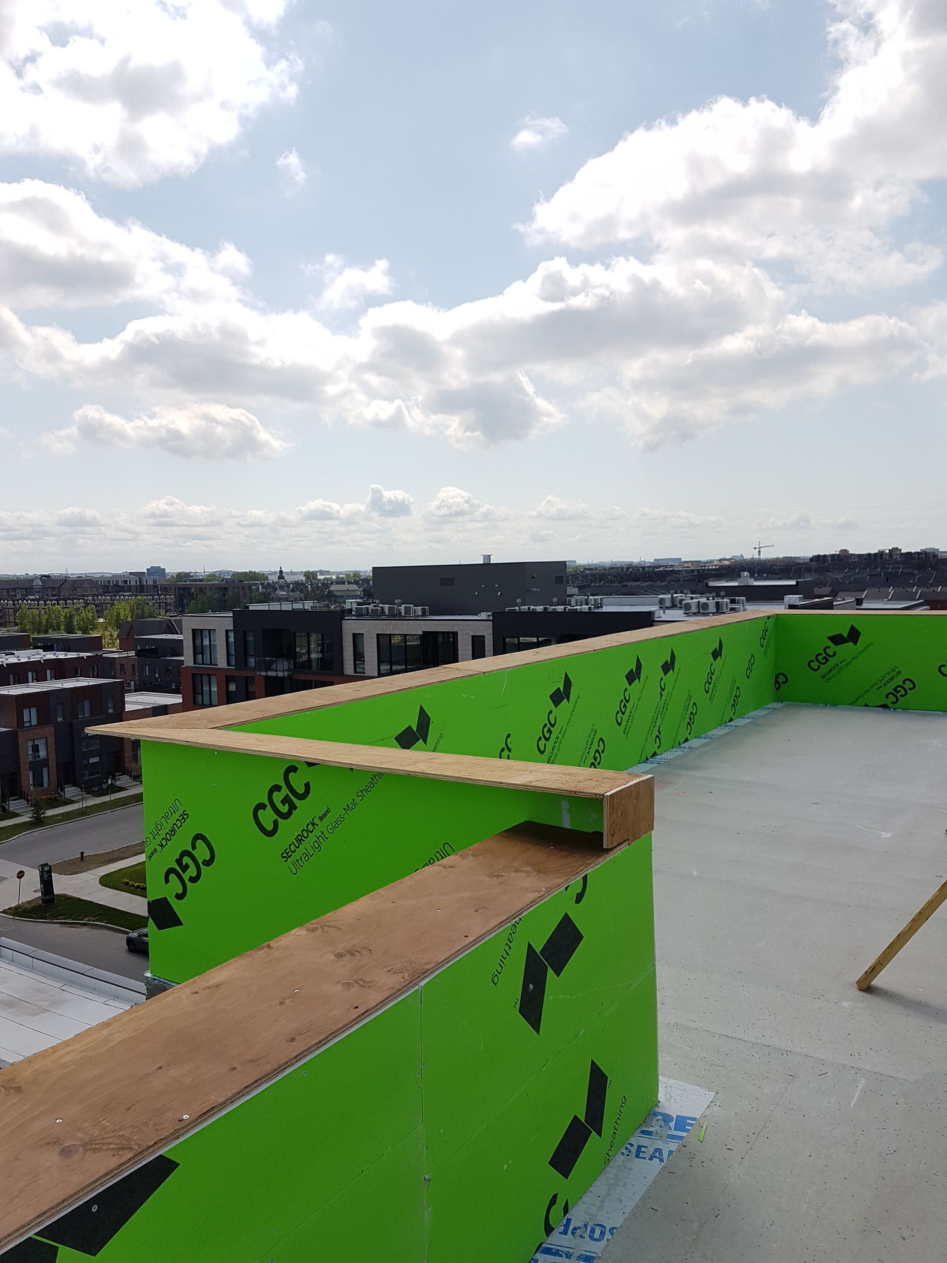 Bâtiment en construction sur un toit, recouvert d'une façade verte et bordé de bois, se détachant sur un ciel nuageux.