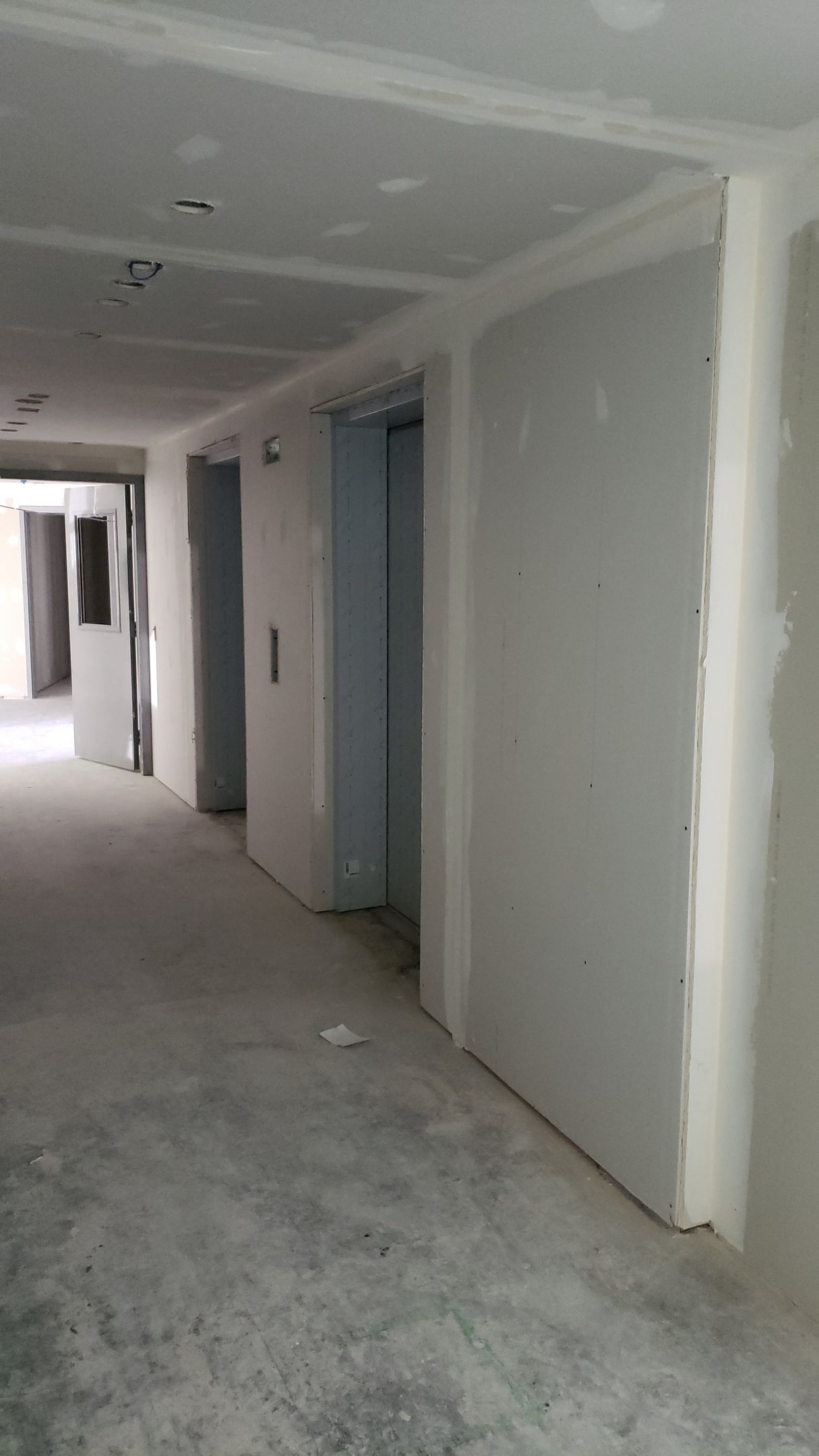 Couloir en travaux avec cloisons sèches non finies aux murs et au plafond ; sol en béton.