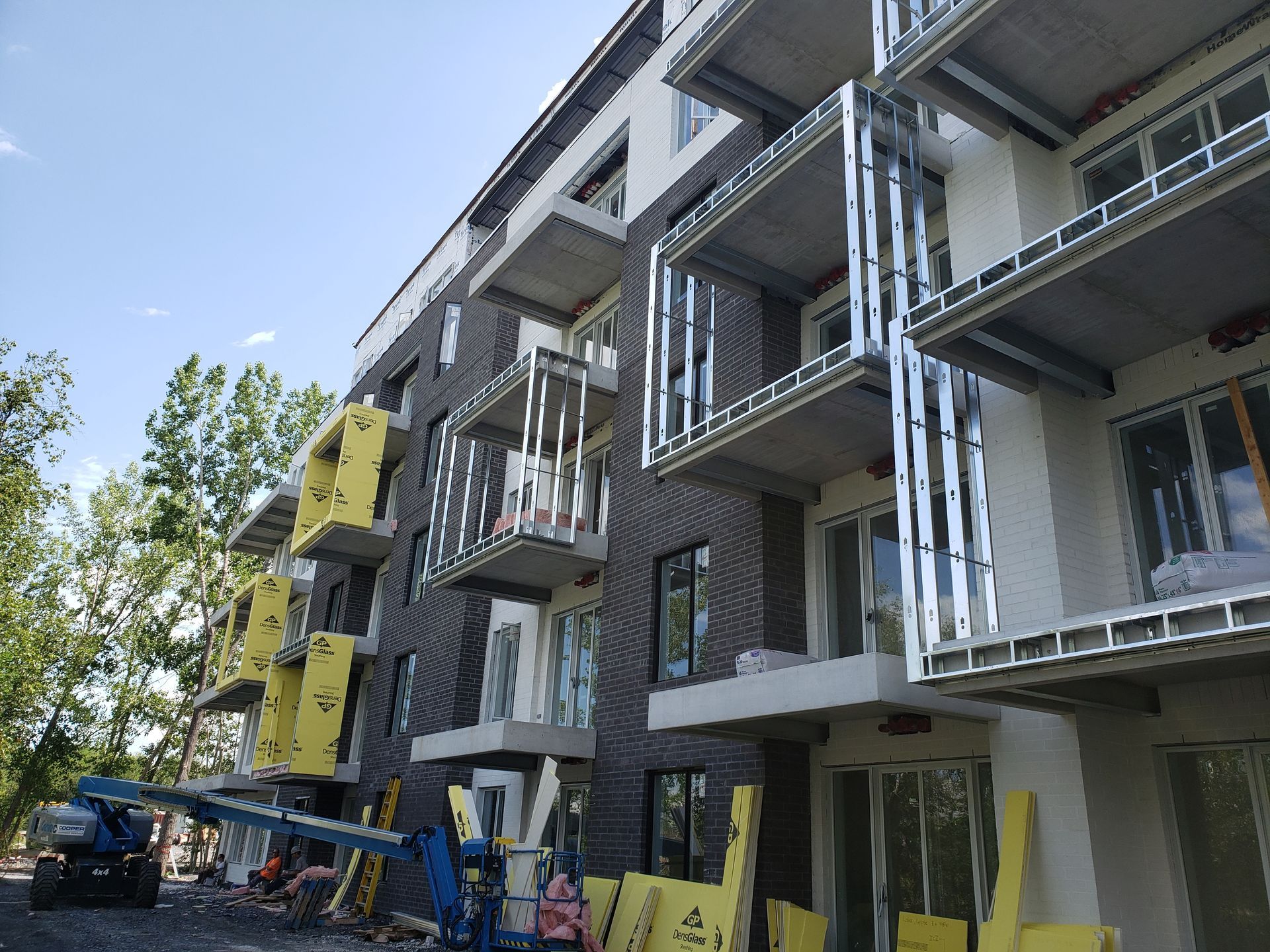 Bâtiment en construction avec des structures de balcons métalliques et un revêtement en briques noires. Isolation jaune visible.