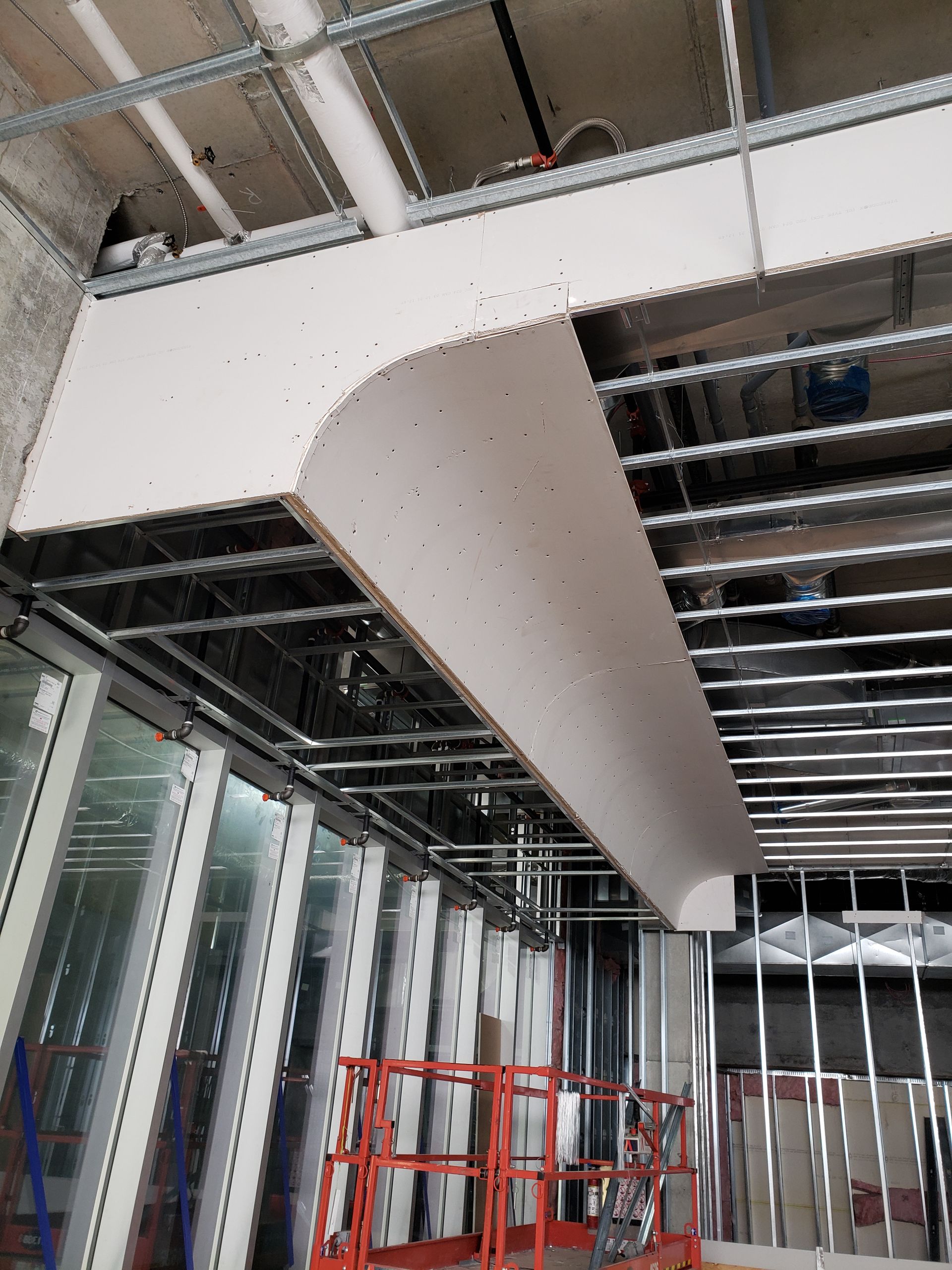 Chantier de construction montrant un soffite en plaques de plâtre sous un plafond avec une ossature métallique et une nacelle élévatrice.