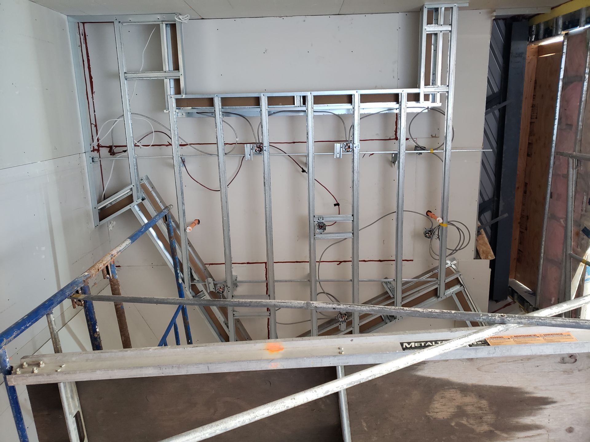 Mur à ossature métallique en construction, avec câblage électrique et plomberie.