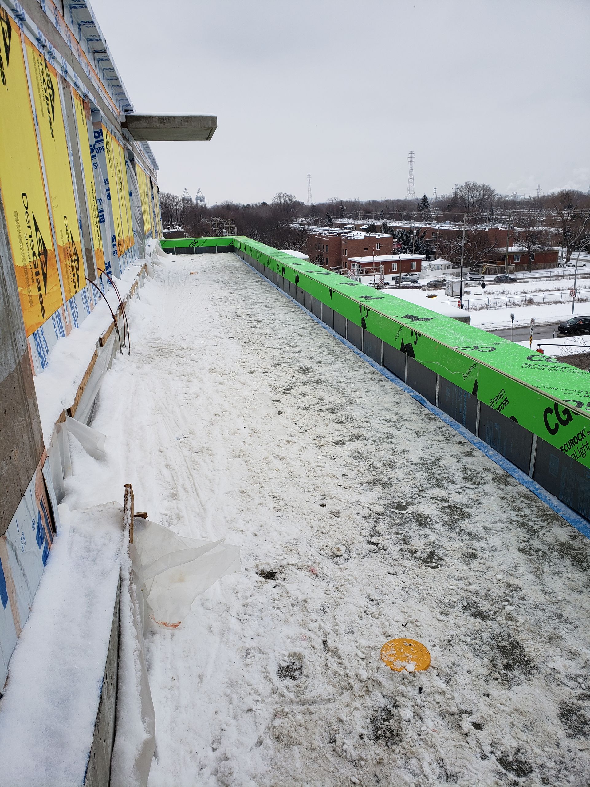 Toit de chantier recouvert de neige, isolation verte, ciel couvert.