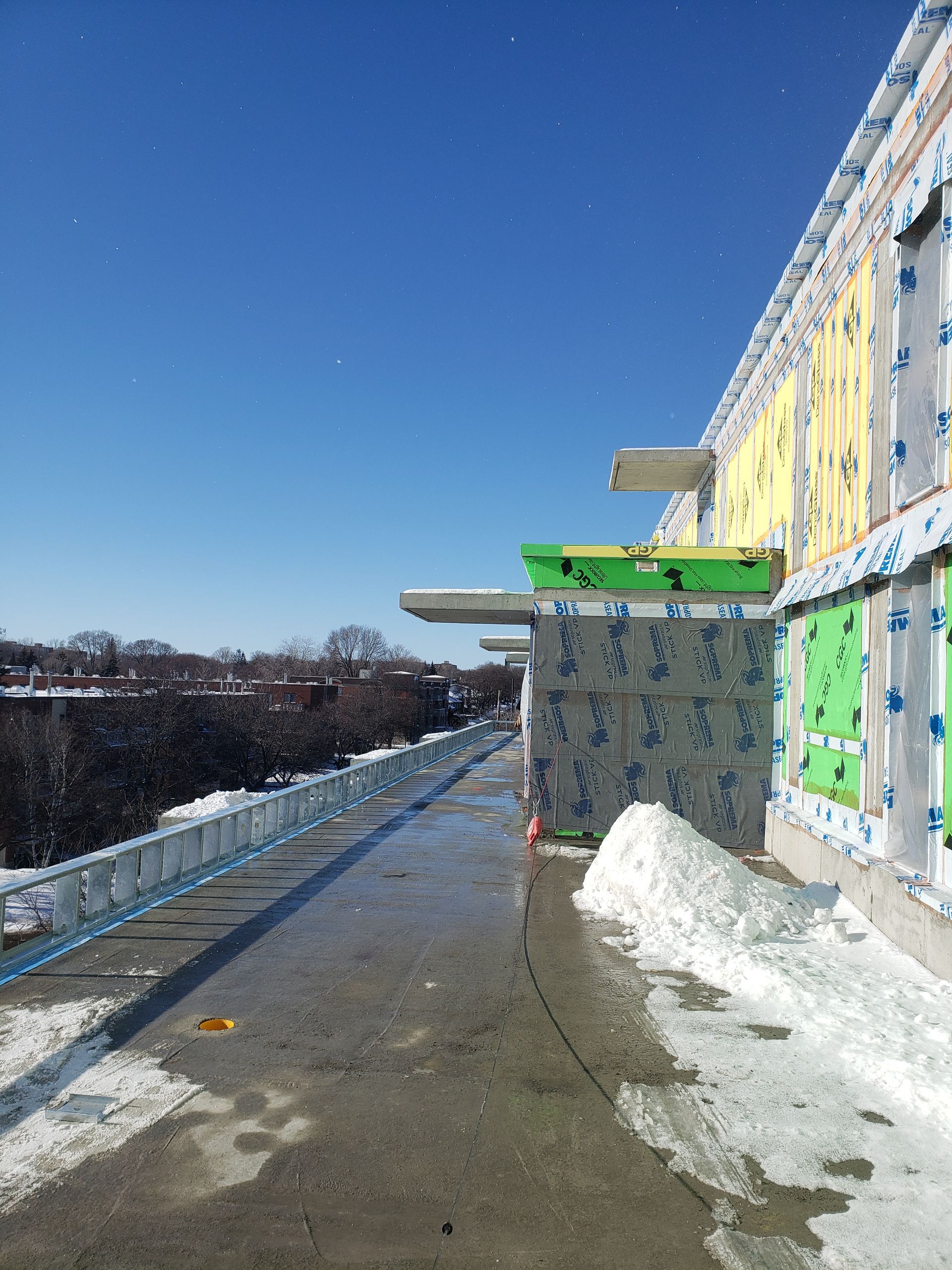 Extérieur d'un bâtiment en construction, isolation apparente, ciel bleu, neige.
