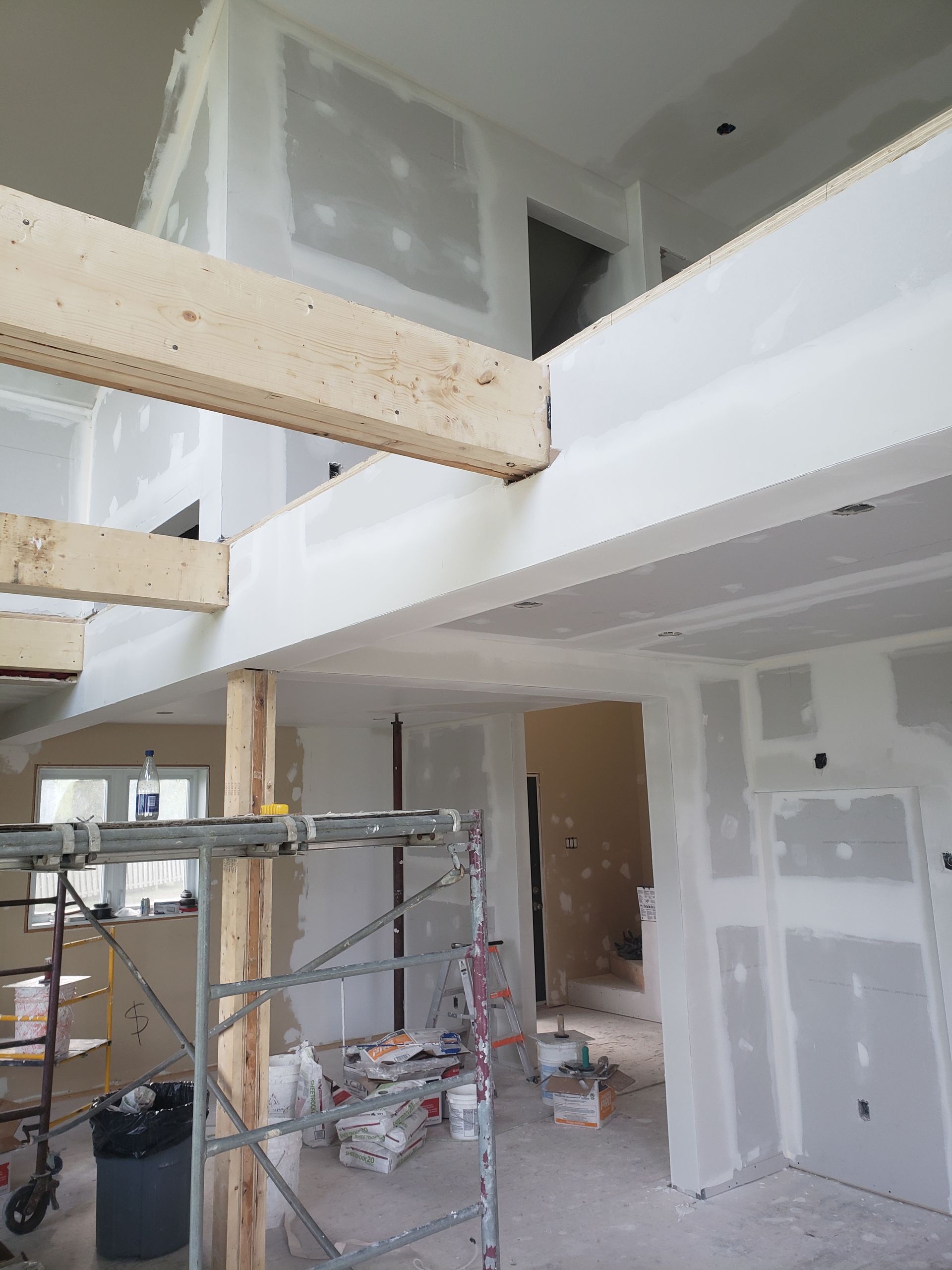 Vue intérieure d'un bâtiment en construction, montrant des cloisons sèches et des poutres en bois apparentes.