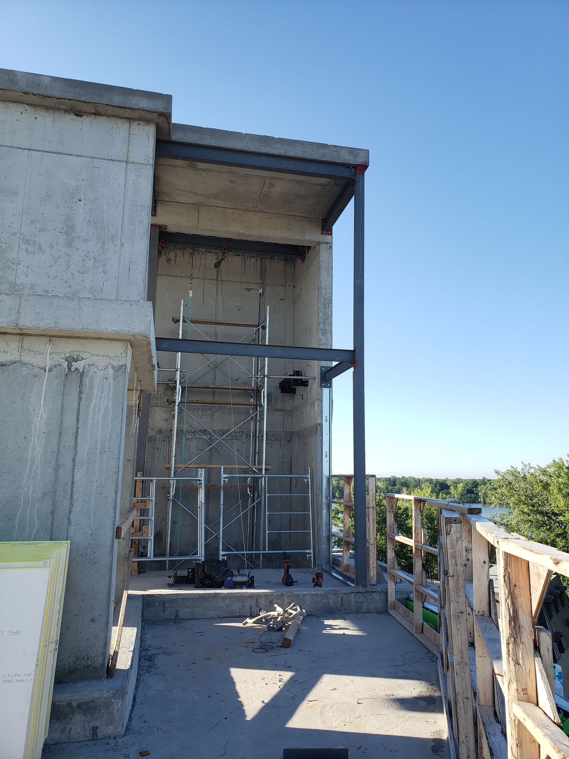 Construction d'un bâtiment aux murs en béton apparent et à la charpente métallique, sous un ciel bleu azur.