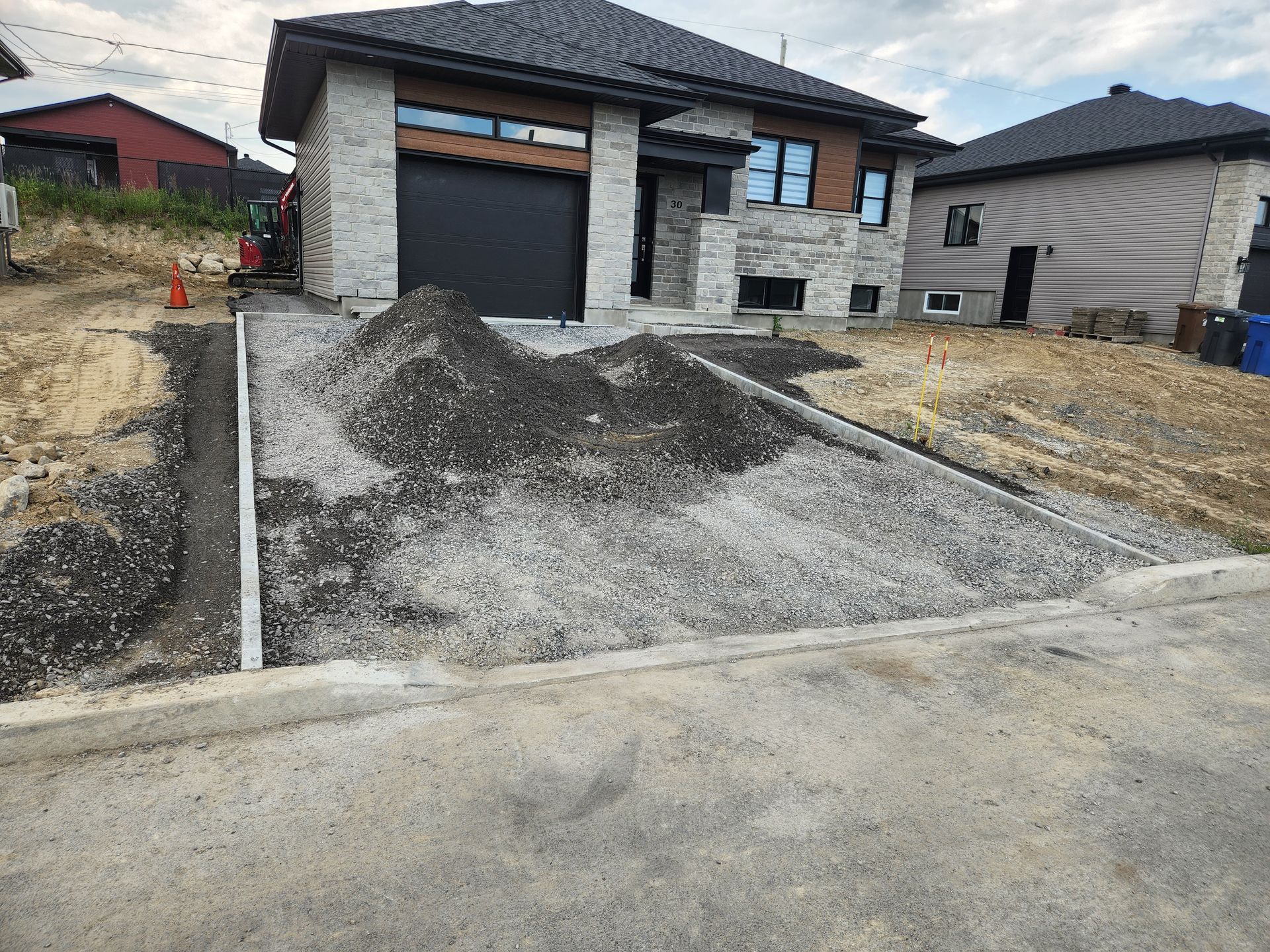 Allée en construction devant une maison moderne, gravier gris, bordure et porte de garage sombre.