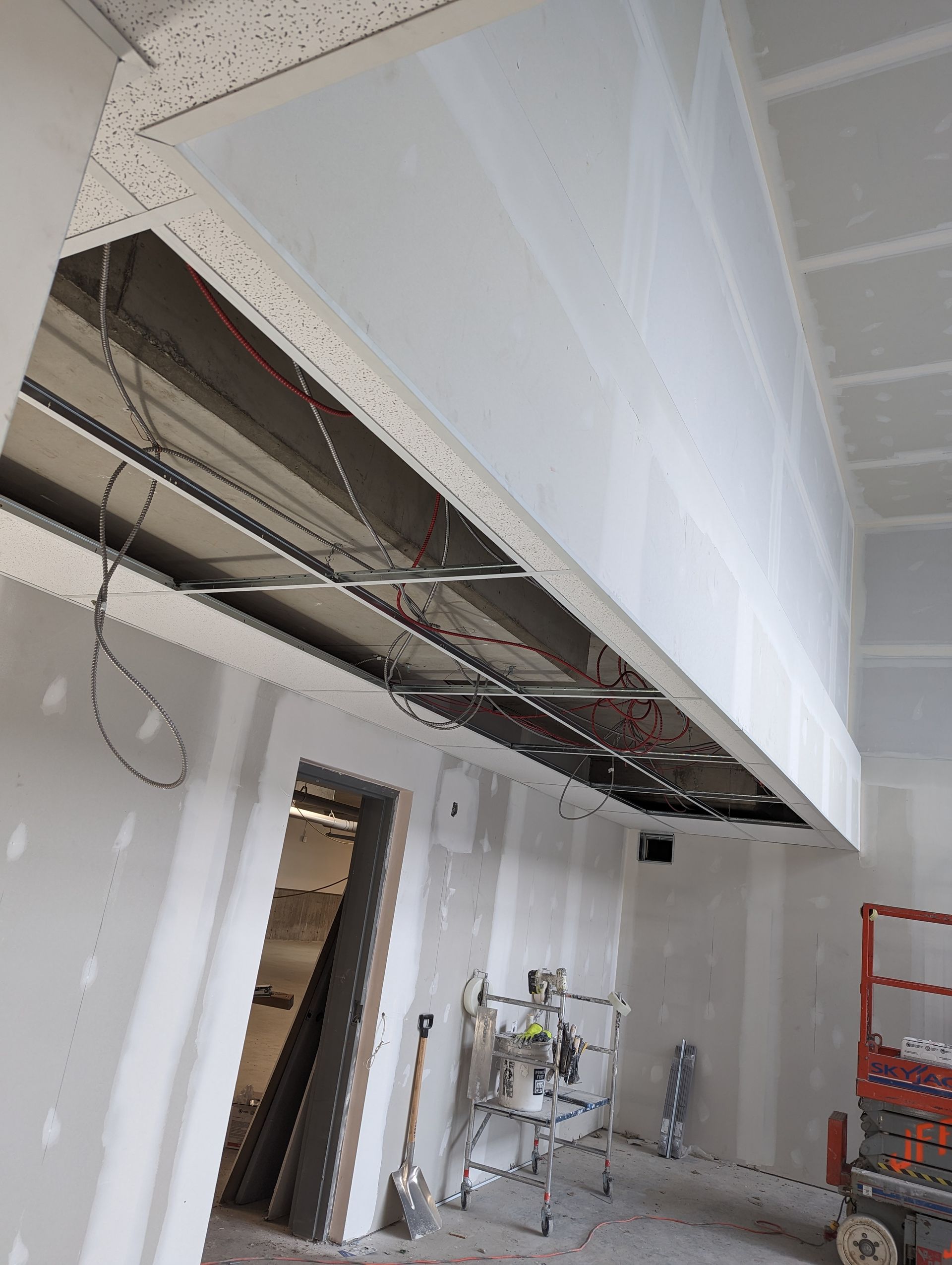 Intérieur d'un chantier de construction avec infrastructure de plafond apparente, cloisons sèches et équipements visibles.