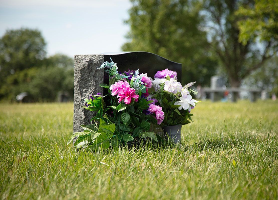 Flower bouquet beside a weathered gravestone in a grassy cemetery
