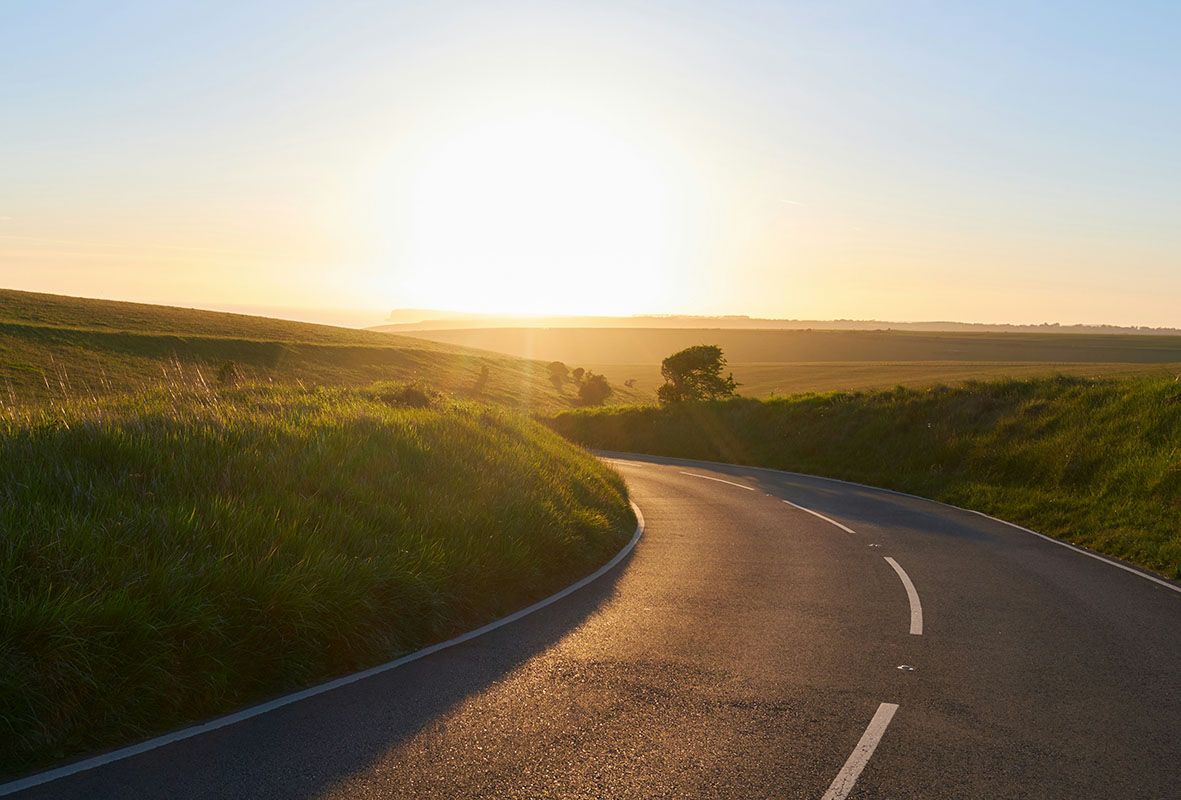 Sunlit winding road through green hills at sunrise