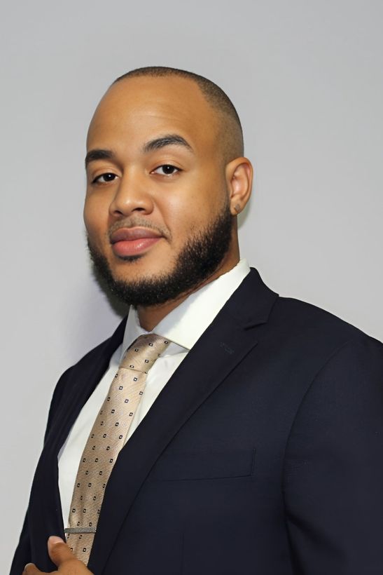 Man in a dark suit and patterned tie posing against a plain gray background