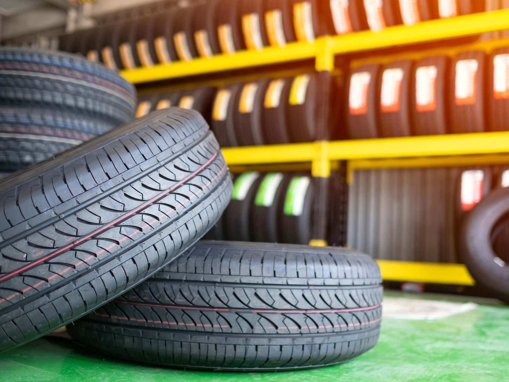 Stack of car tires in front of a shelf filled with various tires at a tire shop.