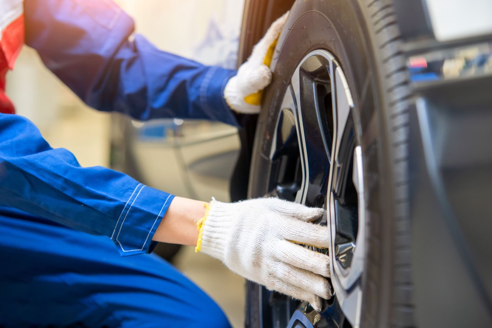Mechanic in blue jumpsuit and gloves inspects a car tire.