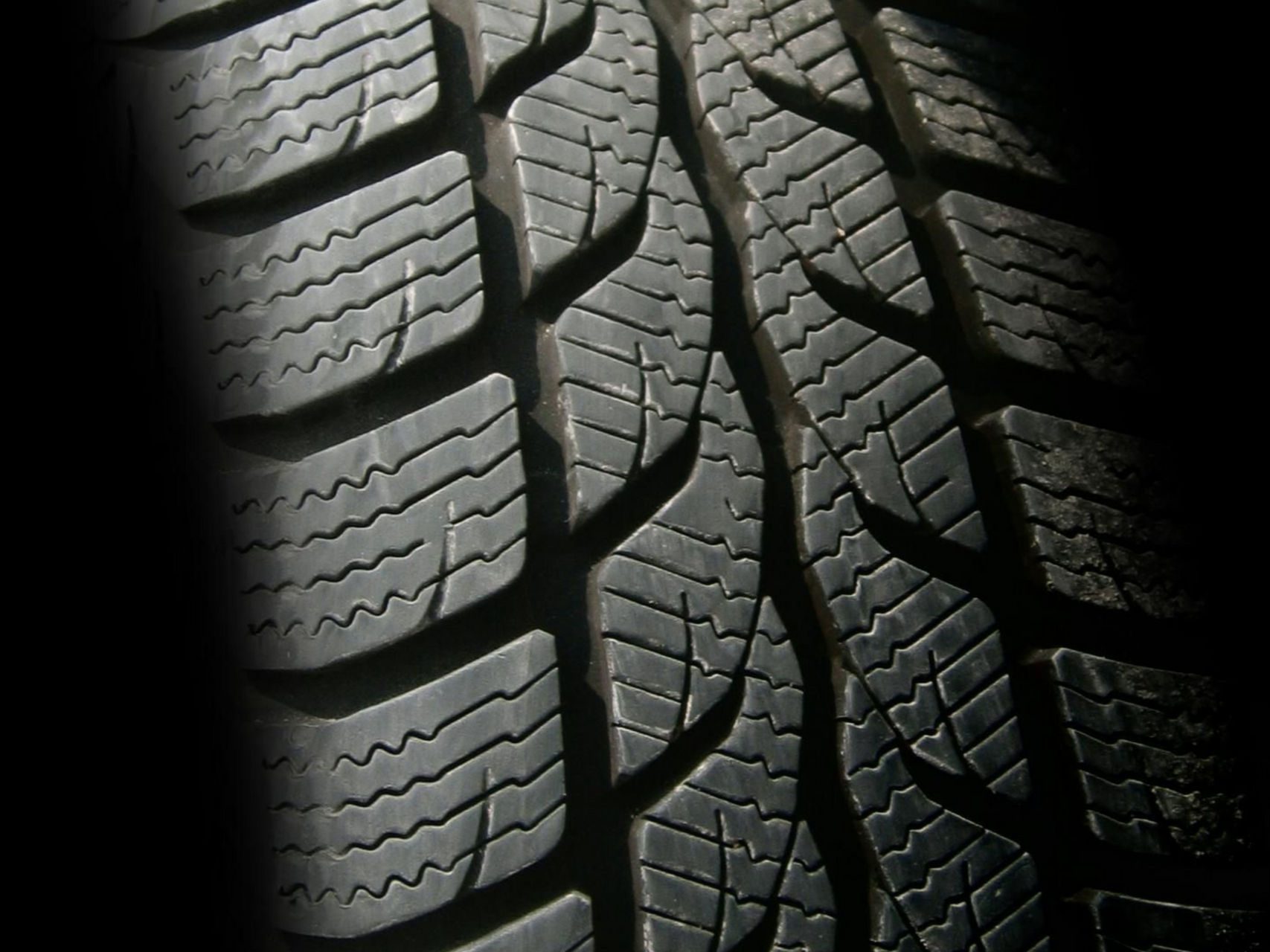 Close-up of a black tire with a complex tread pattern, designed for grip and traction on a road.