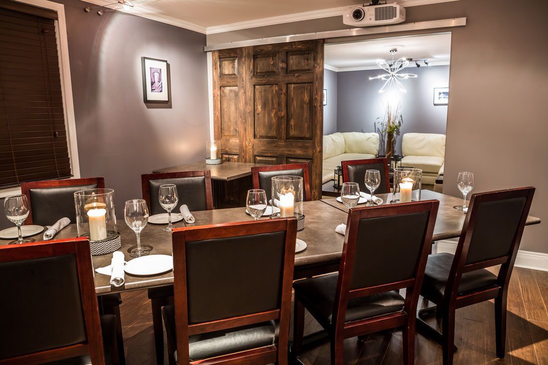 Dining room with a long wooden table set for a meal; a doorway leads to a living room.