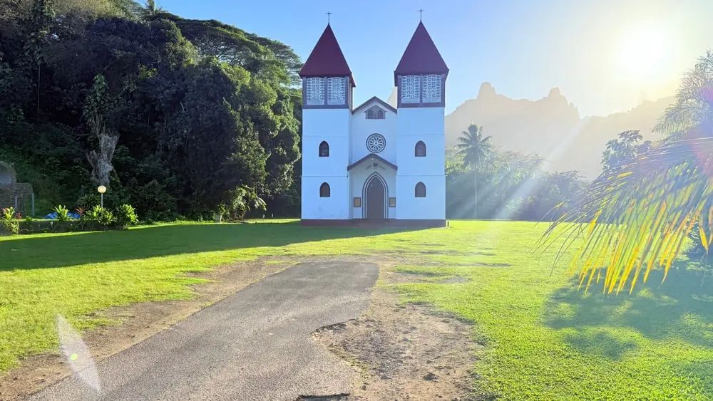 White church with twin red-roofed towers on a sunny green hillside, with a path leading to the entrance