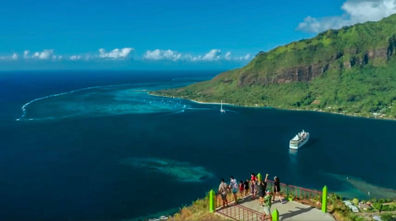 Scenic ocean bay with green cliffs, a small boat, and tourists at a lookout point