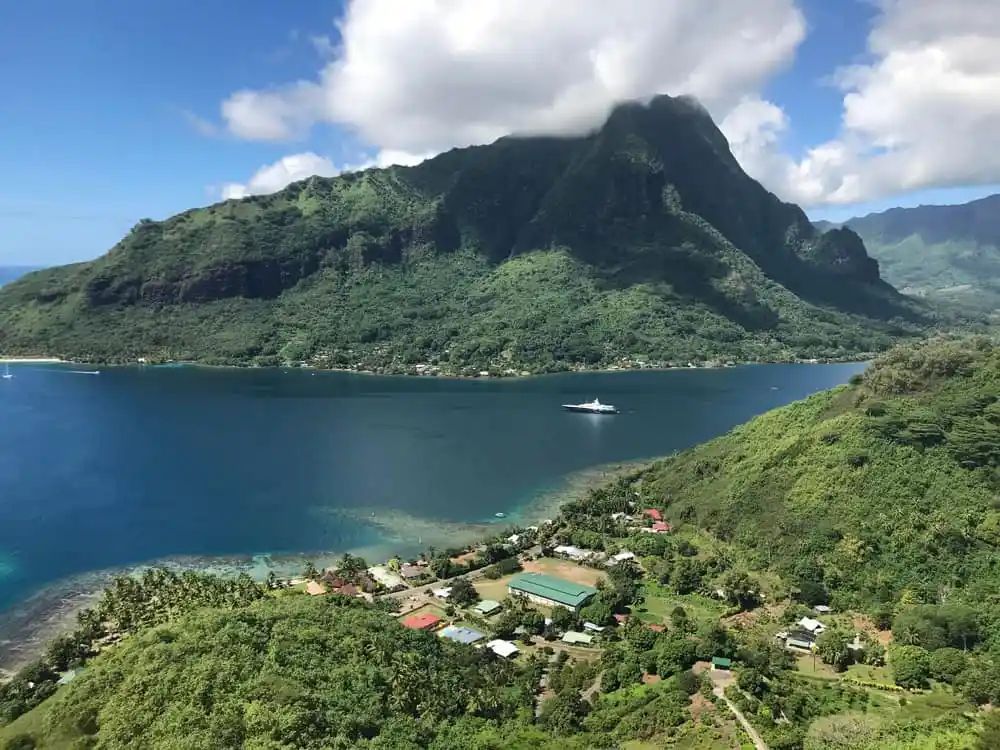 Lush green coastal mountain overlooking blue bay with a small boat and seaside village