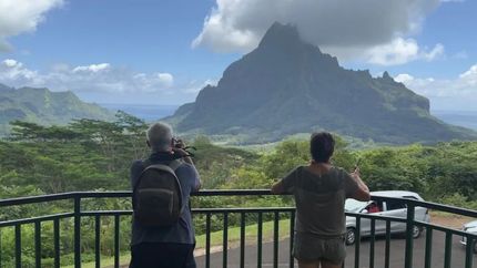 Two people overlooking a tropical mountain landscape from a scenic viewpoint on a cloudy day