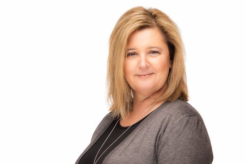 Portrait of a smiling woman with blonde hair wearing a gray cardigan against a white background