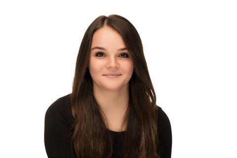 Portrait of a person with long brown hair, wearing a black top, smiling against a white background