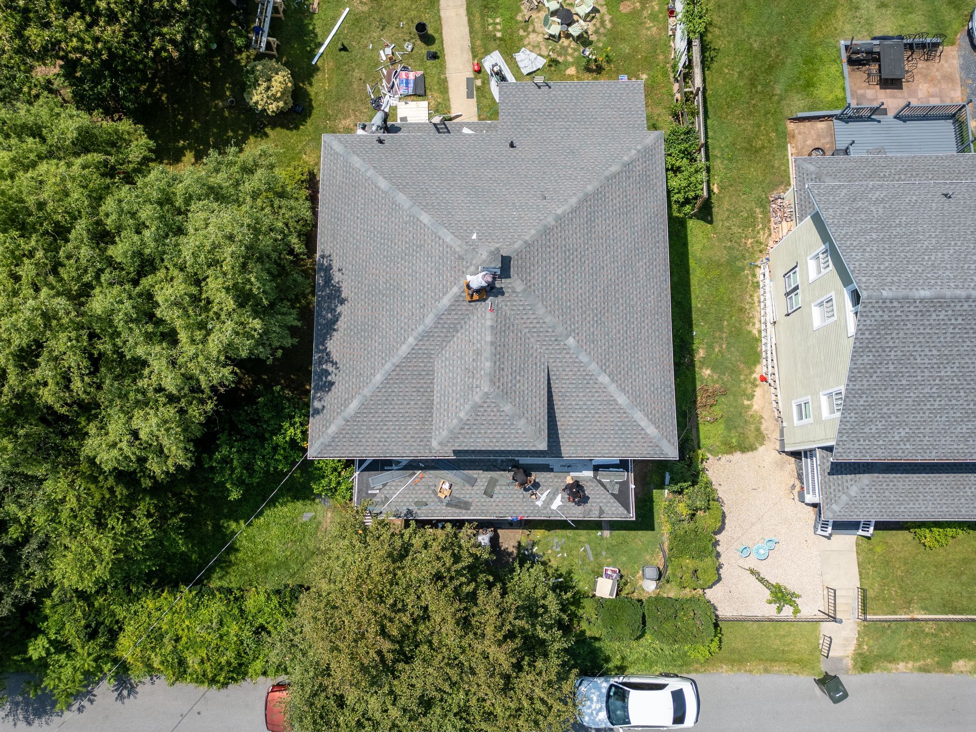 Crew working on a hip roof section with tear-off material staged in the yard