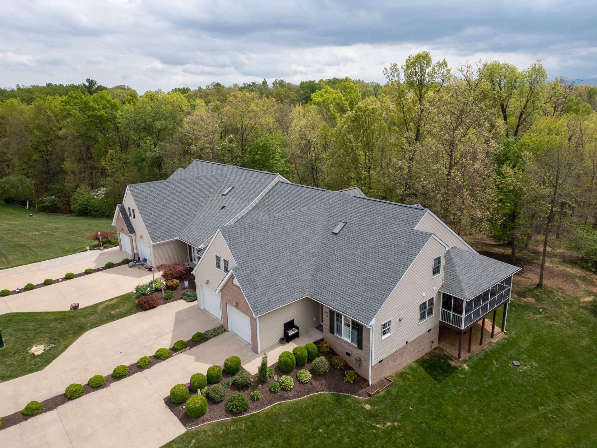 Aerial view of a large gray-roofed suburban house surrounded by trees and a landscaped driveway