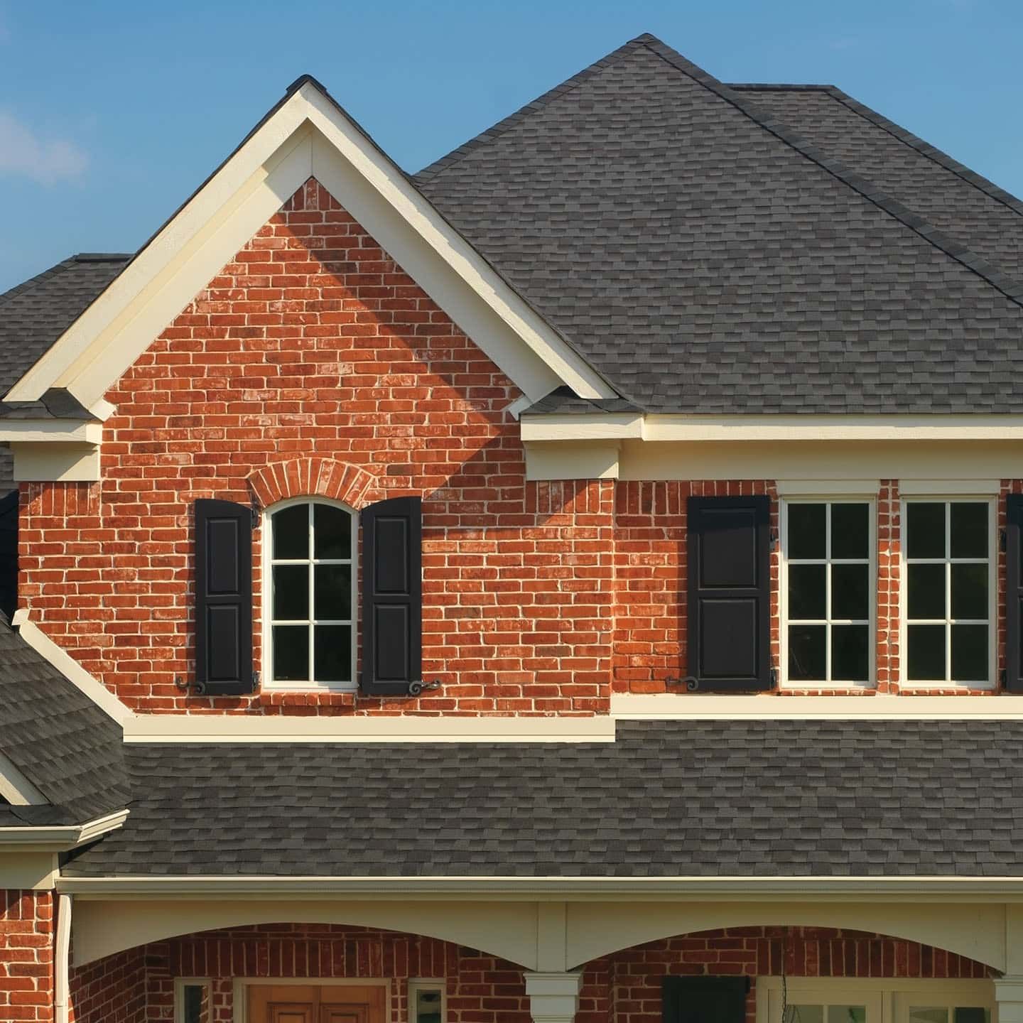 Brick house exterior with gray shingle roof, black shutters, and white trim