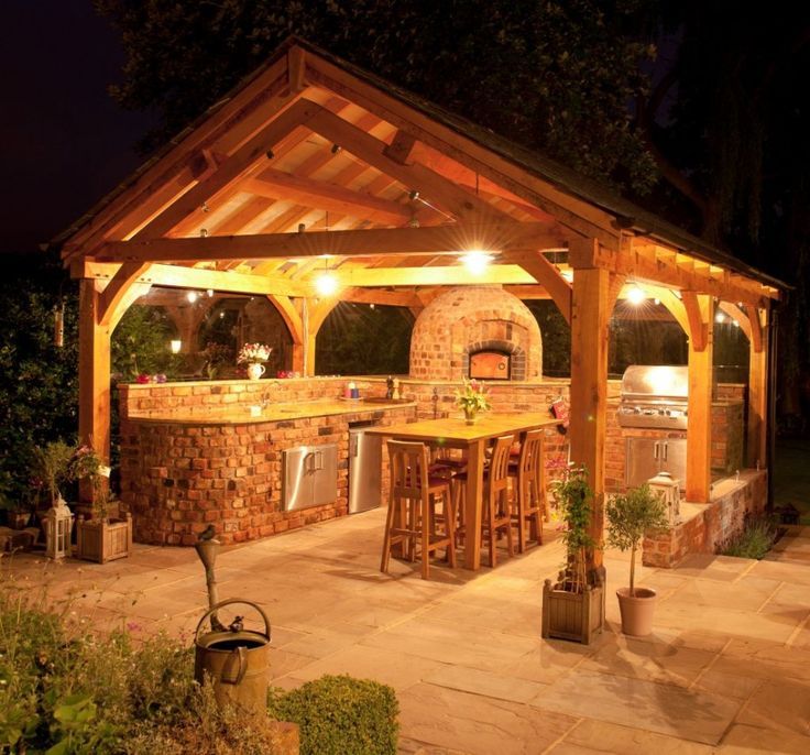 Illuminated outdoor wooden gazebo bar with brick grill and high stools at night