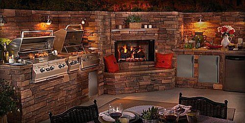 Cozy outdoor kitchen with brick grill, stone fireplace, and dining table lit by warm ambient lights