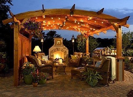 Cozy outdoor patio with wooden pergola, string lights, fireplace, and wicker seating at dusk