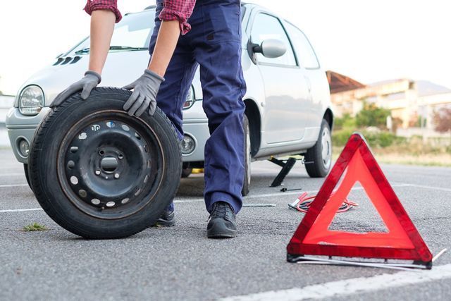A man is changing a tire on a car next to a red triangle.