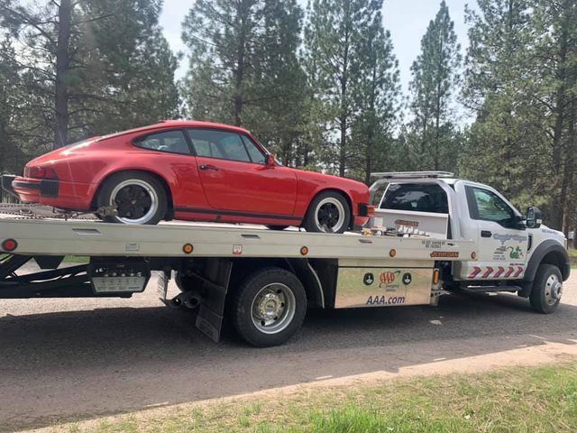 A red porsche is being towed by a tow truck.