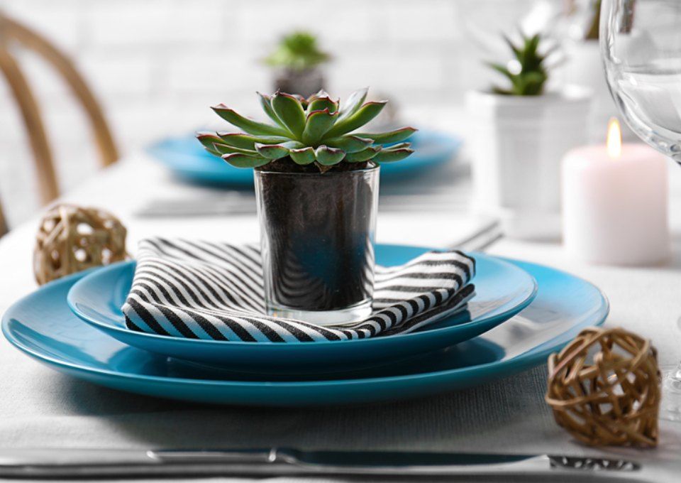 A table setting with teal plates, a black and white striped napkin, a potted succulent, and a candle on a white tablecloth.