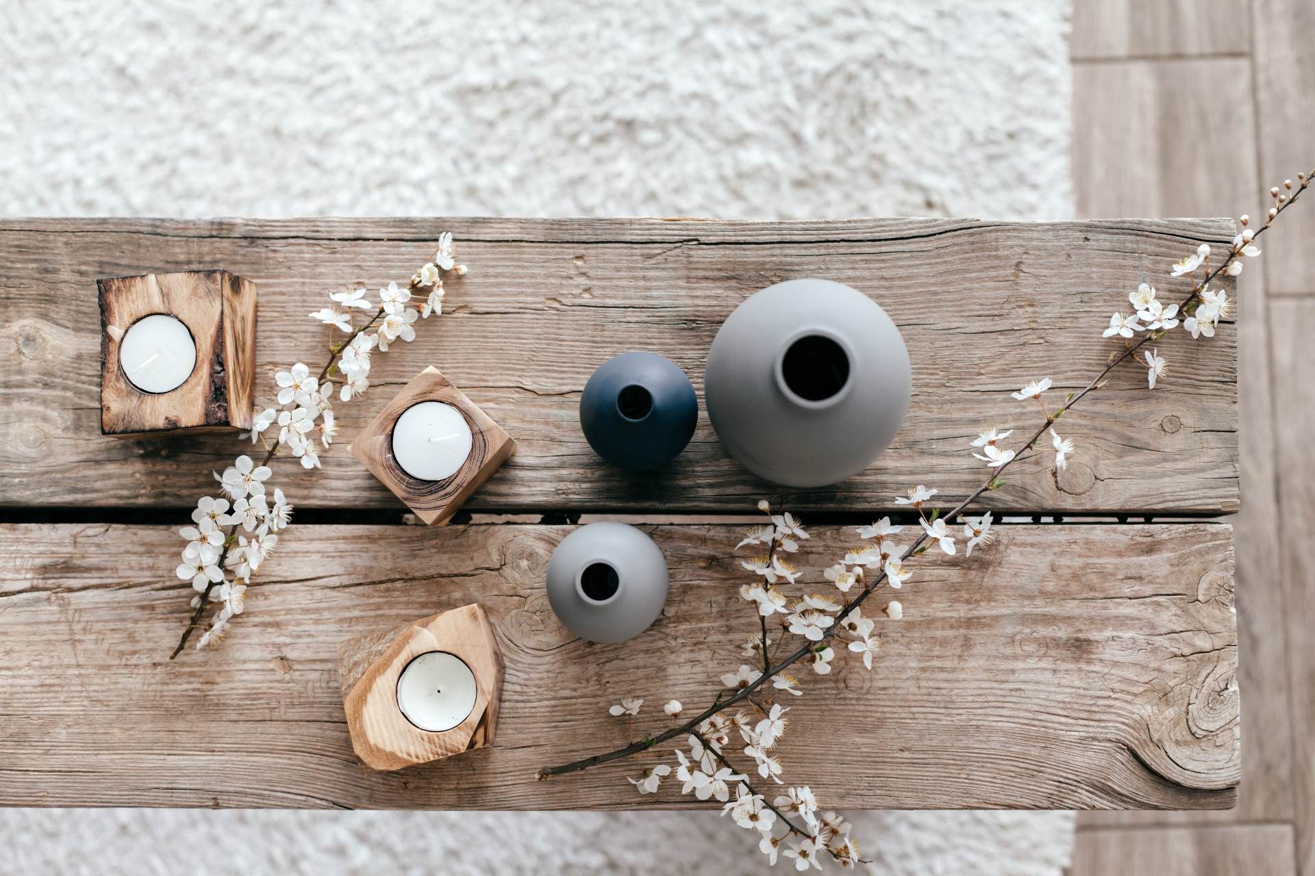 A rustic wooden coffee table decorated with ceramic vases, wooden candle holders, and delicate white flowering branches.