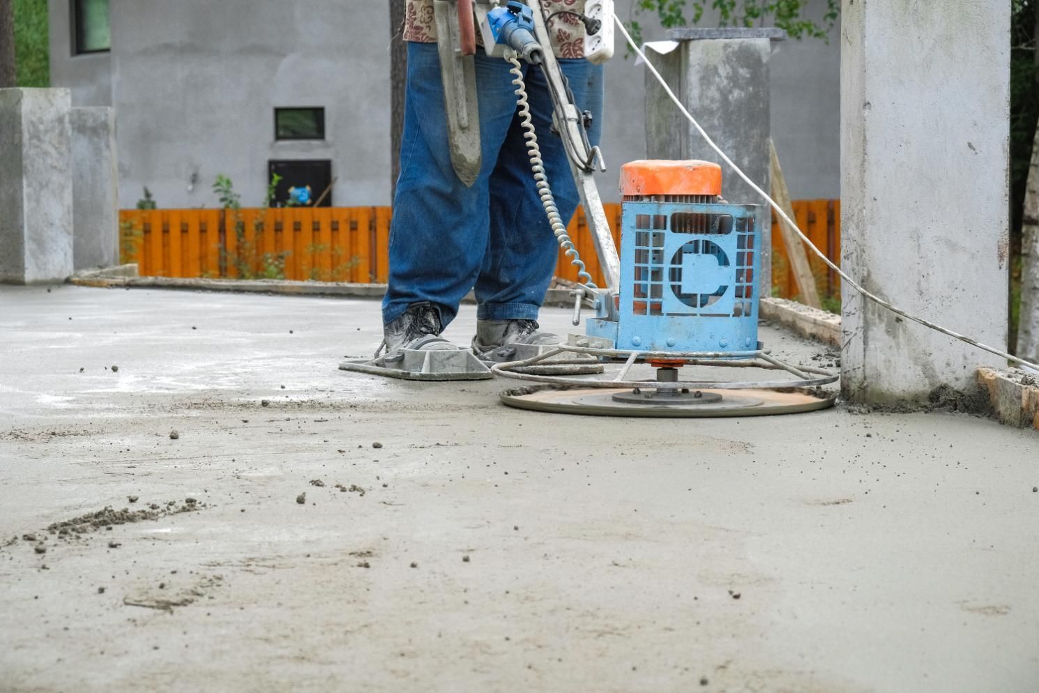 Person using a concrete grinder on a concrete surface. Blue grinder, blue jeans, outdoors.
