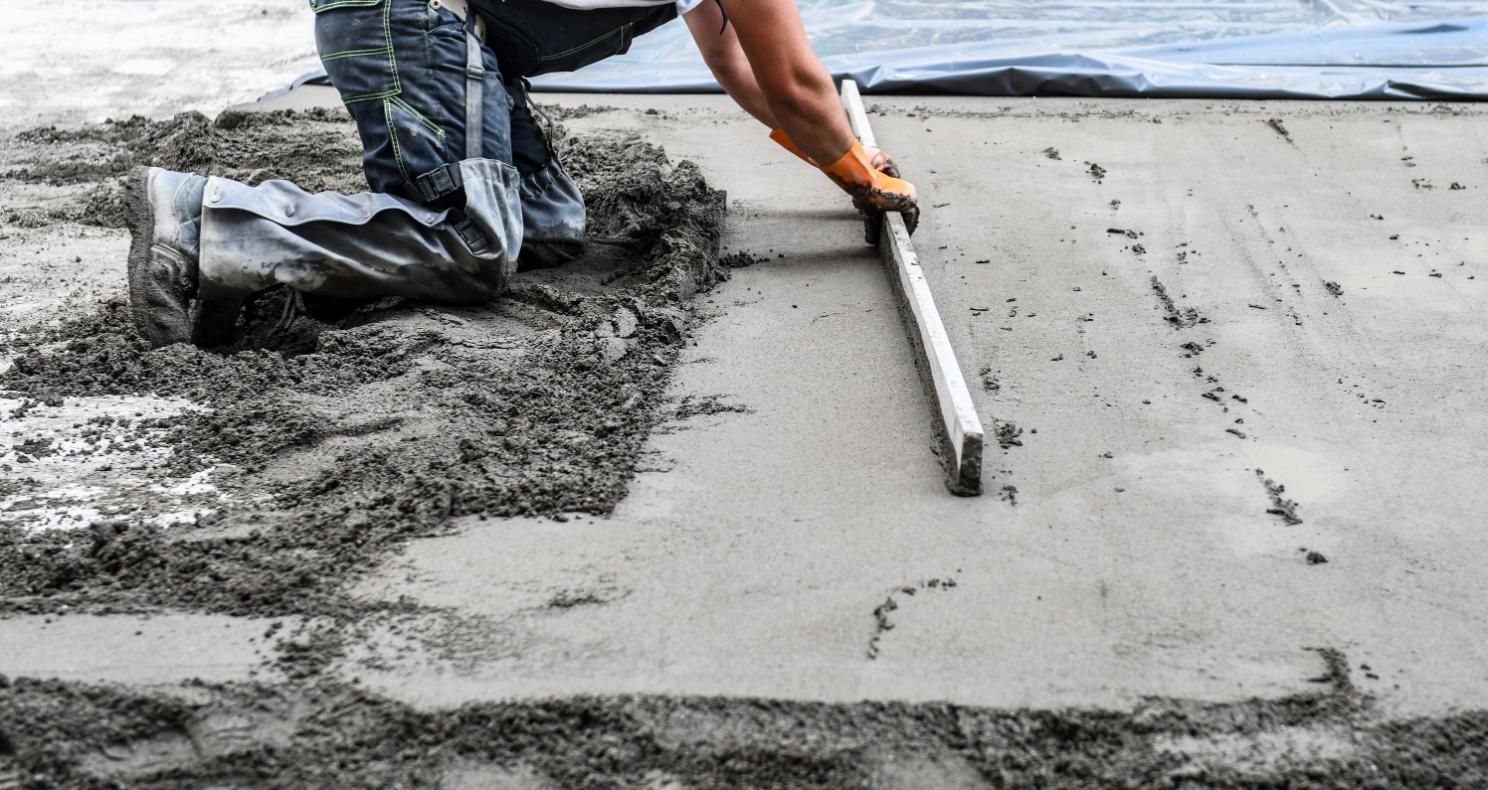 Construction worker leveling wet cement with a screed.