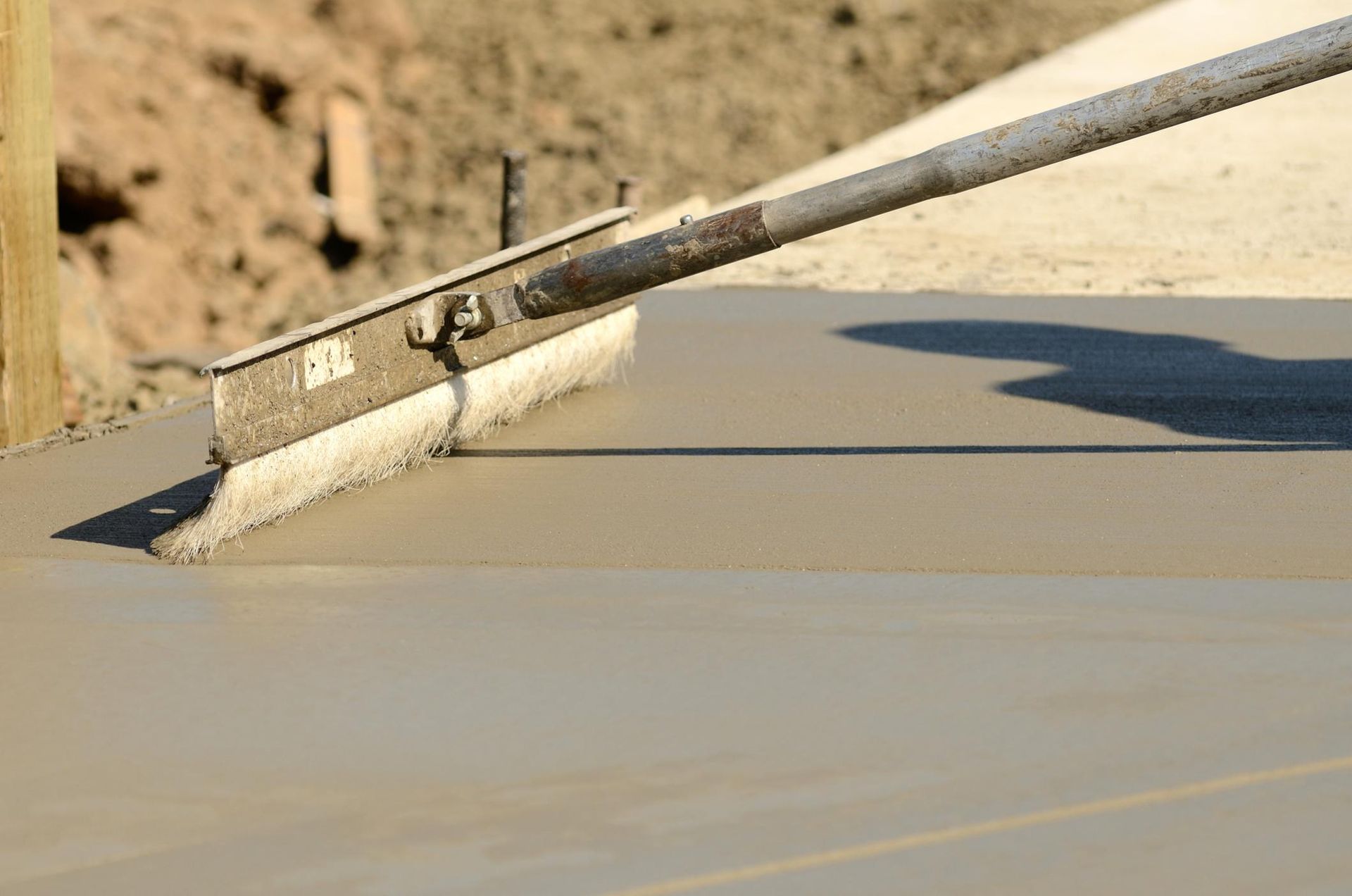 A worker uses a broom to texture a freshly poured concrete slab.