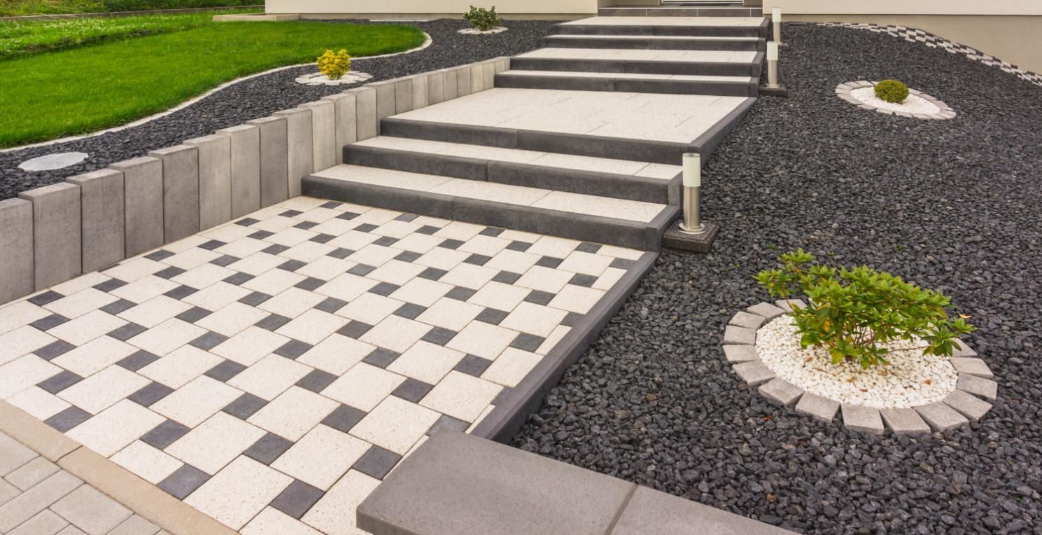 Steps and pathway with gray and white pavers, bordered by dark stones and greenery.