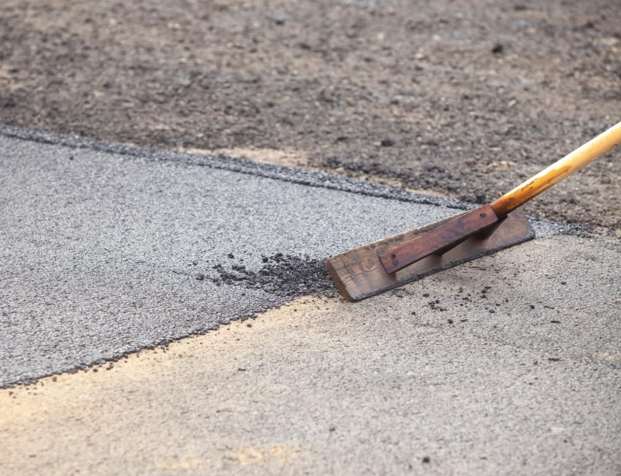 A worker smoothing asphalt with a wooden lute.
