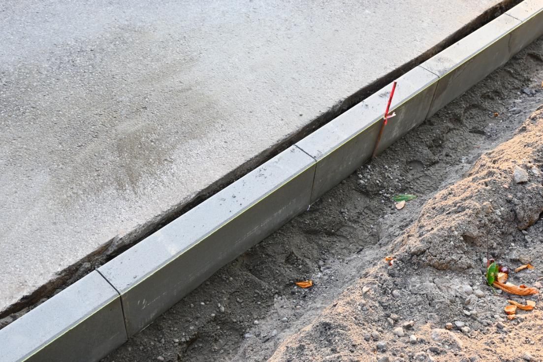 Concrete curb alongside a paved surface and dirt. A red marker is visible.