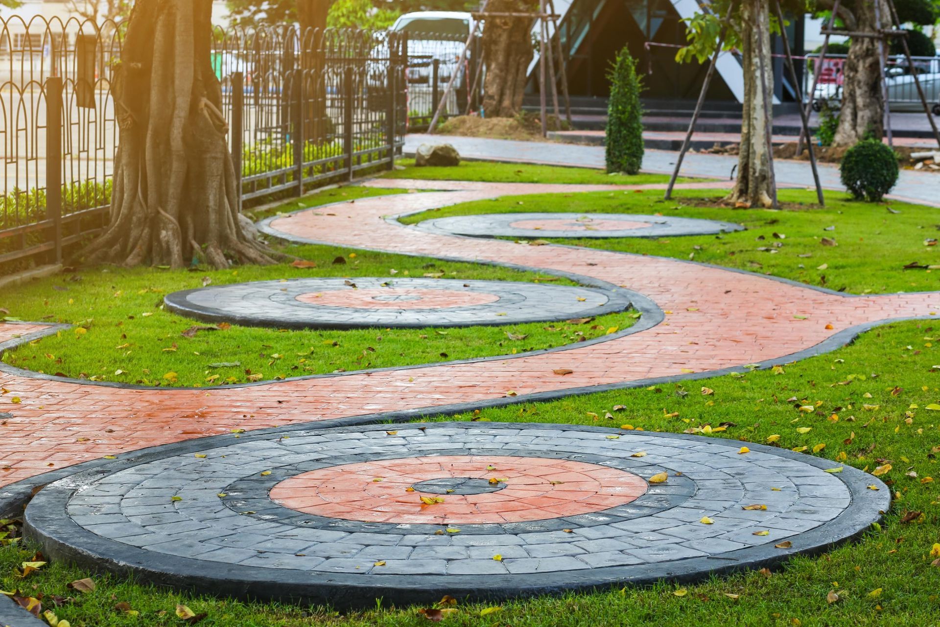 Winding red and grey stone path through a green lawn with circular decorative platforms, trees, and landscaping.