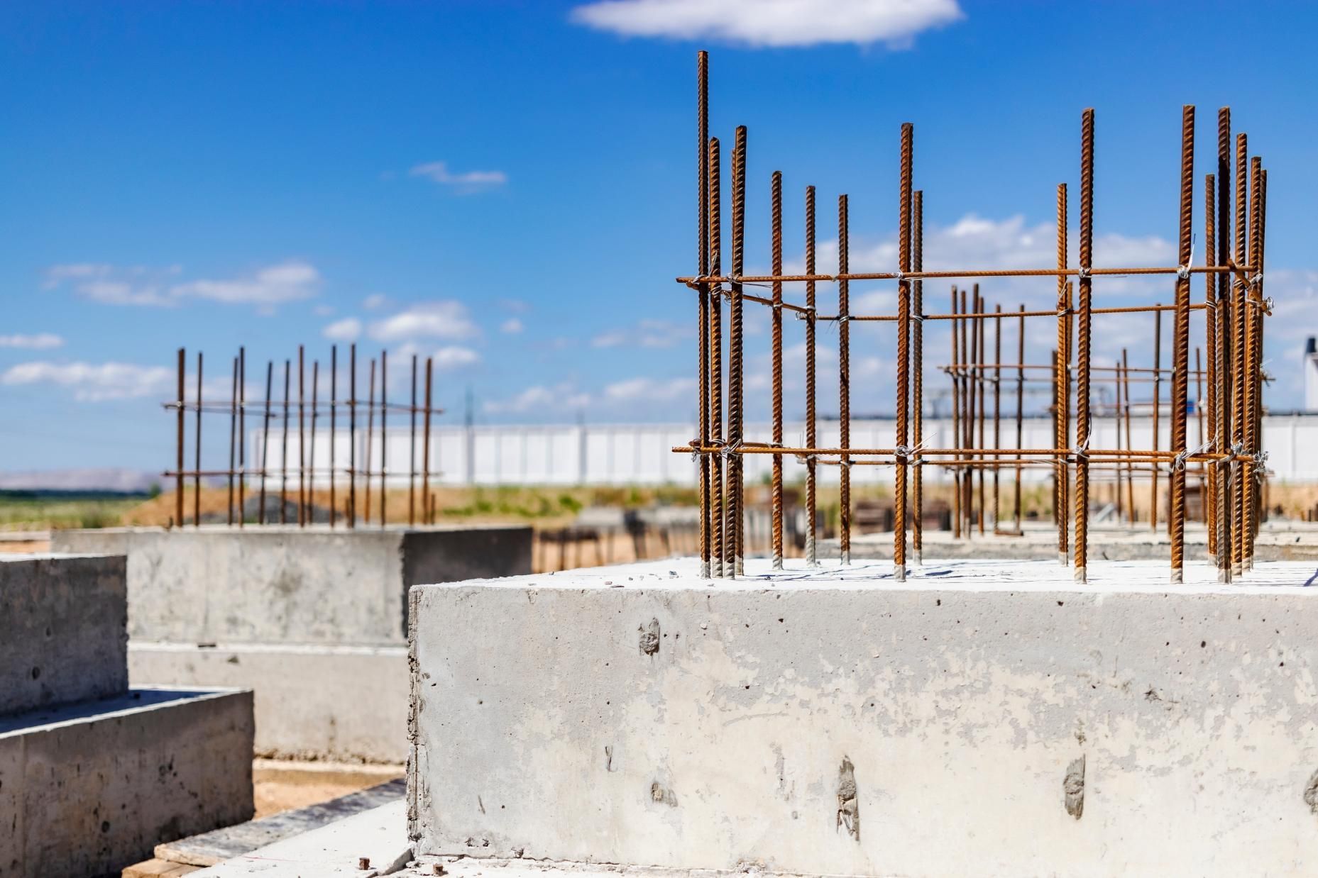 Concrete pillars with exposed steel reinforcement bars on a construction site, under a blue sky.