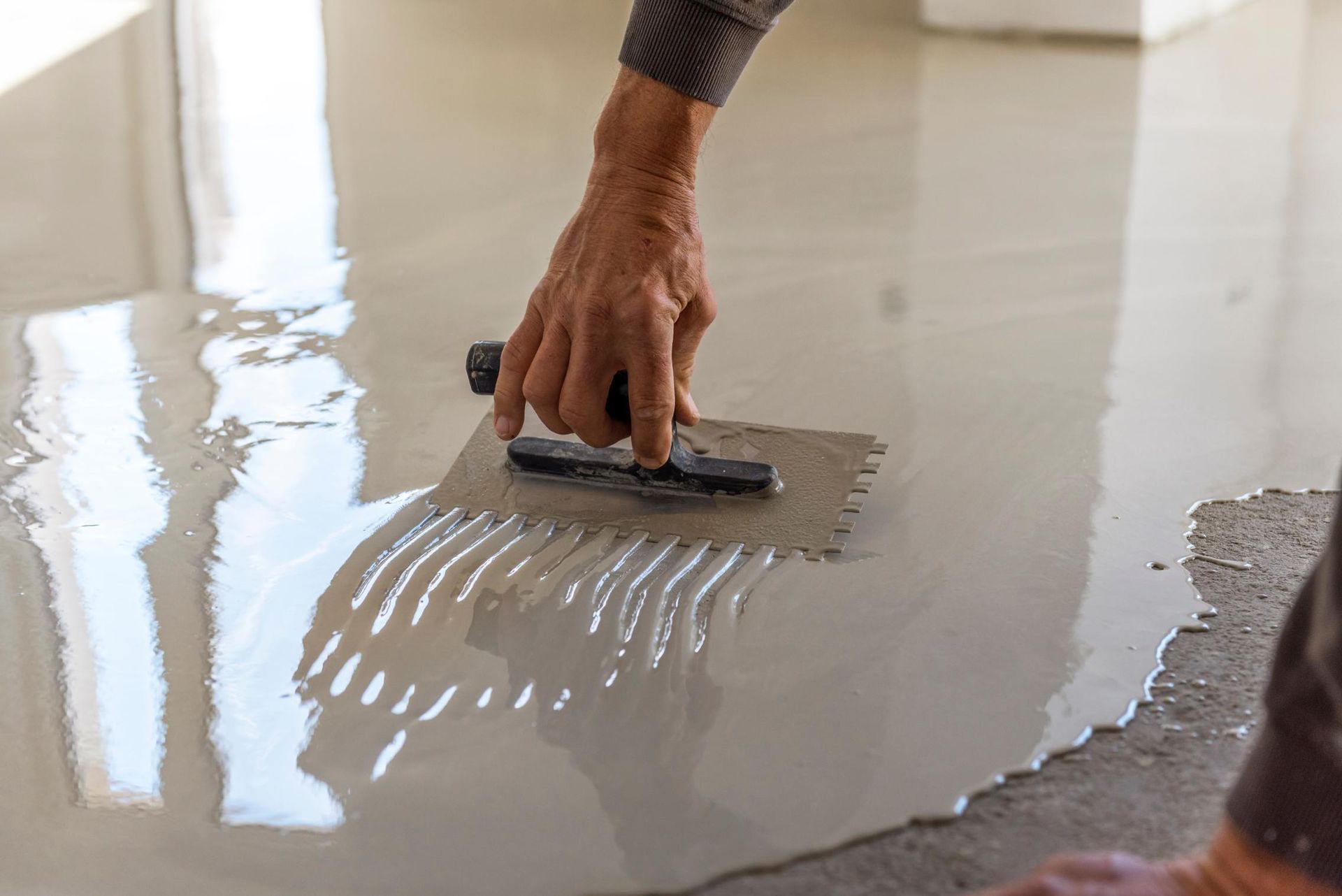 Person using a notched trowel to spread wet concrete on a floor.
