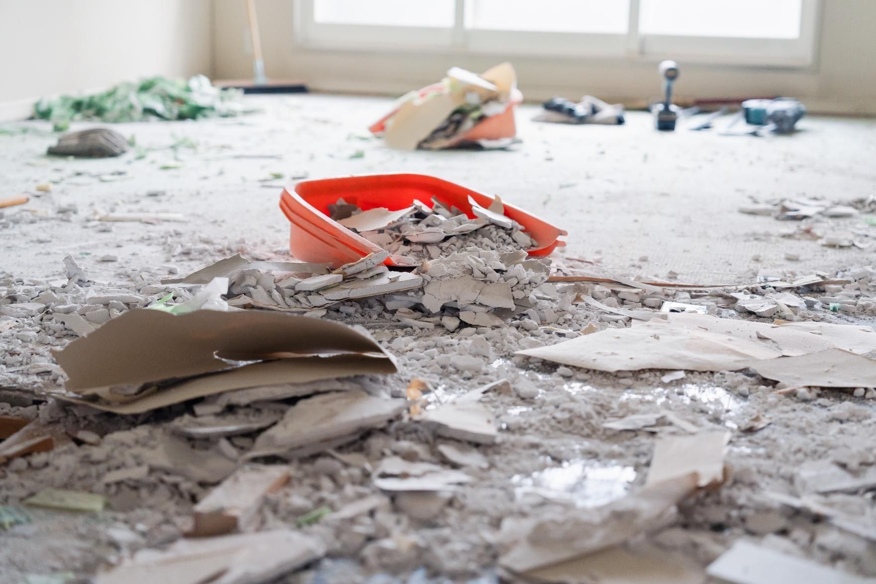 Demolition debris scattered on a floor, with an orange dustpan.
