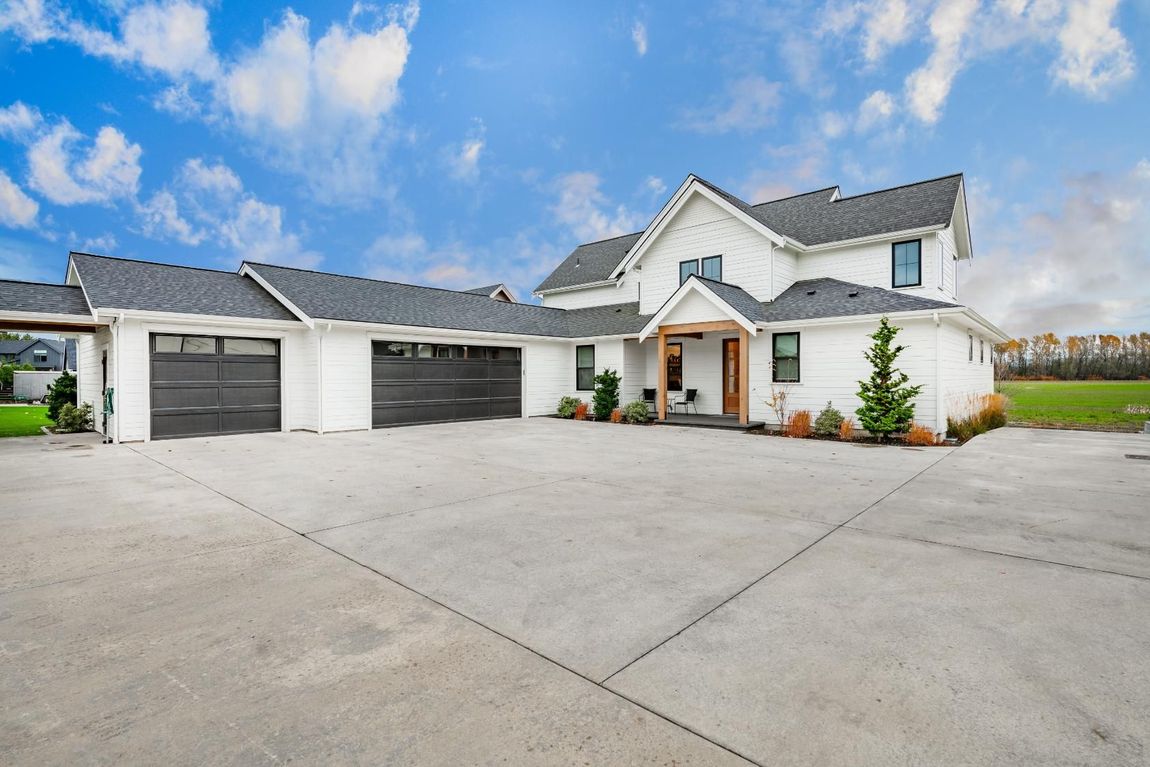 White farmhouse with a large driveway, three-car garage, and a blue sky.