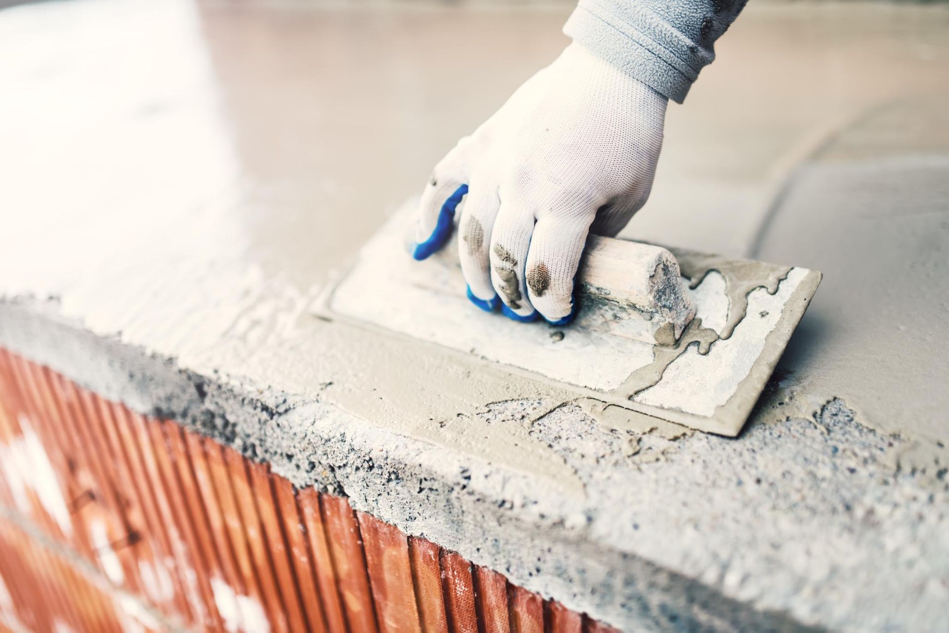 A person wearing gloves using a trowel to smooth wet cement on a brick surface.
