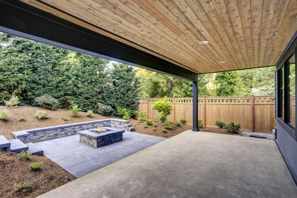 Covered patio with fire pit, gray concrete floor, wooden ceiling, and a wooden fence.