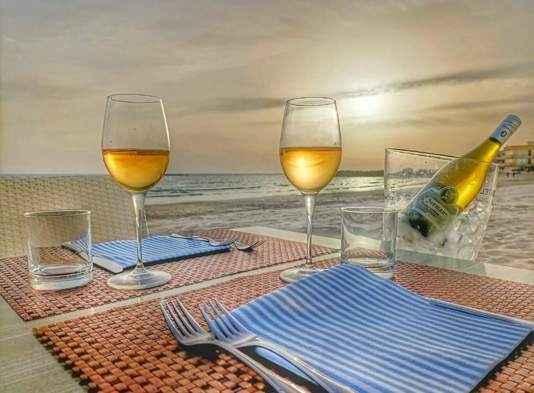 Tavolo apparecchiato per due sulla spiaggia: bicchieri da vino.